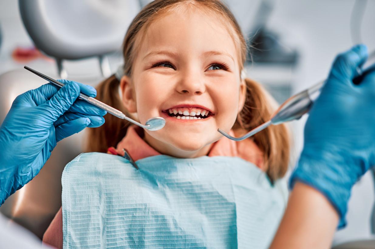 A kid at the dentist smiling and having her teeth looked at