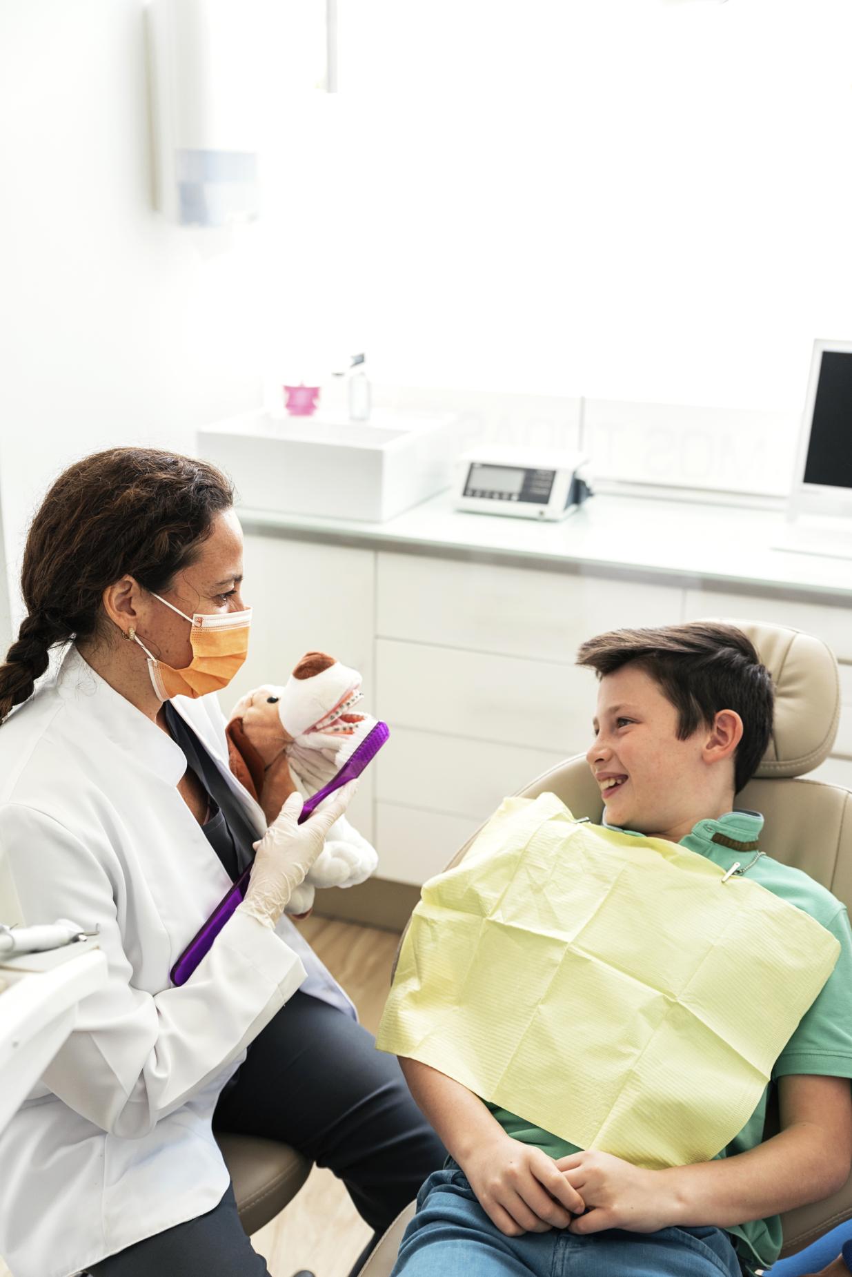A female dentist with a kid in a dental exam chair smiling