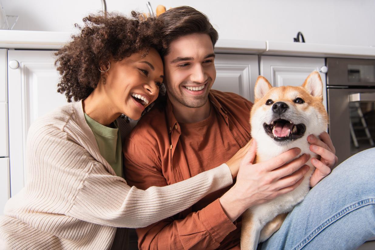 A happy male and female couple with a dog smiling together and sitting down, petting the dog