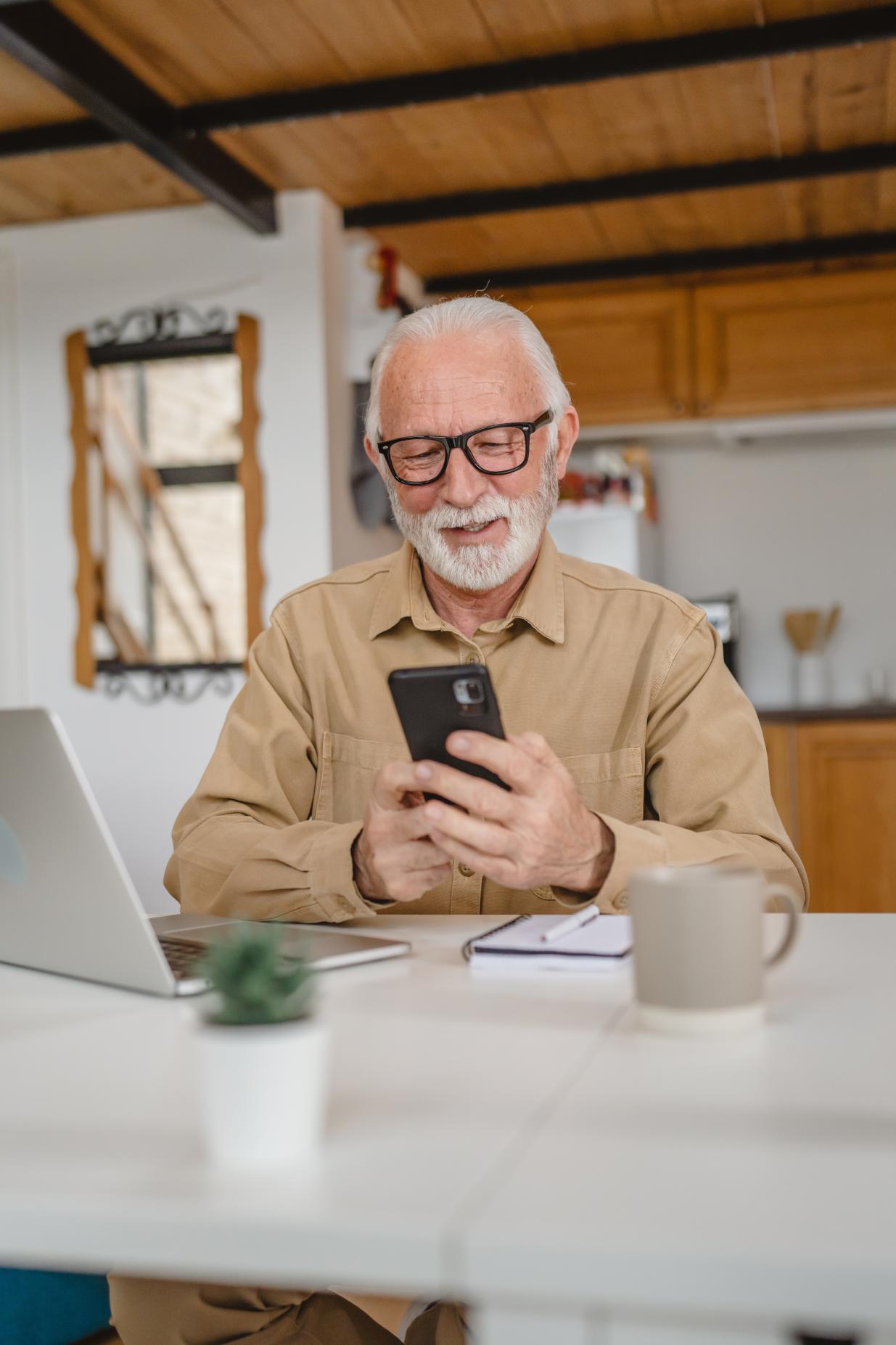 Happy senior man wearing glasses while interacting with his phone screen.