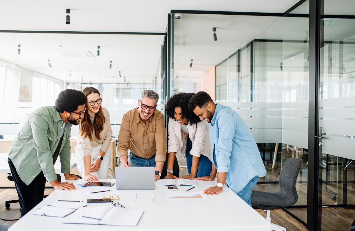 A group of people standing around a laptop in a conference room