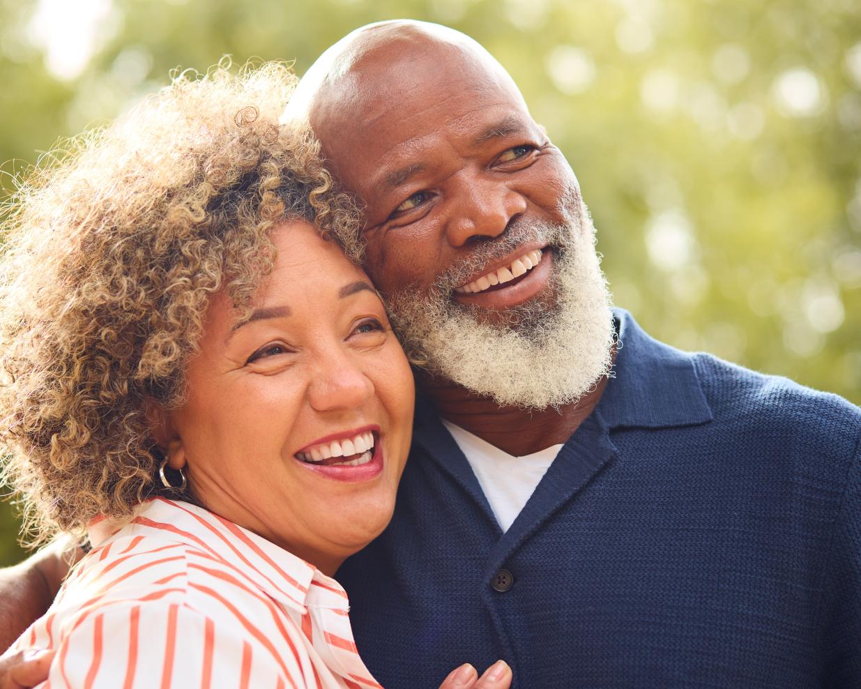 Happy couple embracing one another while smiling and looking off into the distance.