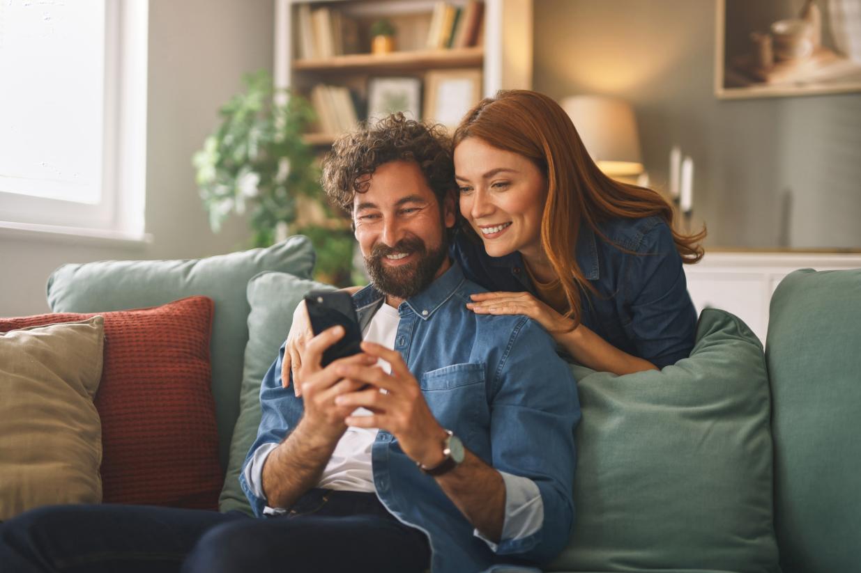 A male and female couple sitting on a couch together looking at a cellphone