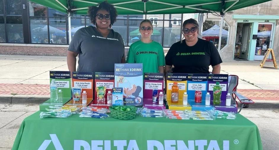 Happy Delta Dental employees volunteering at event and standing behind a table with a Rethink Your Drink kit.