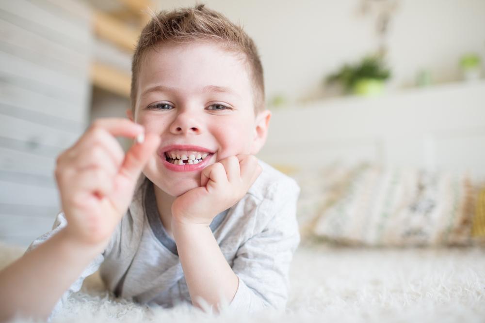 Happy young boy holding up his baby tooth.