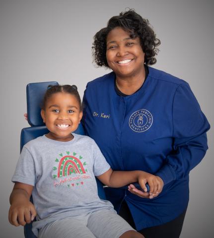 A female dentist sits with a child patient smiling in dental exam chair