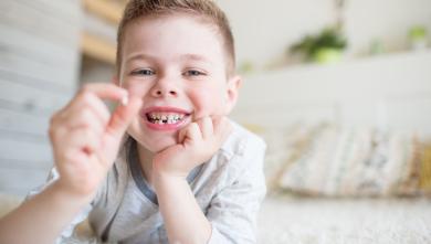 Happy young boy holding up his baby tooth.