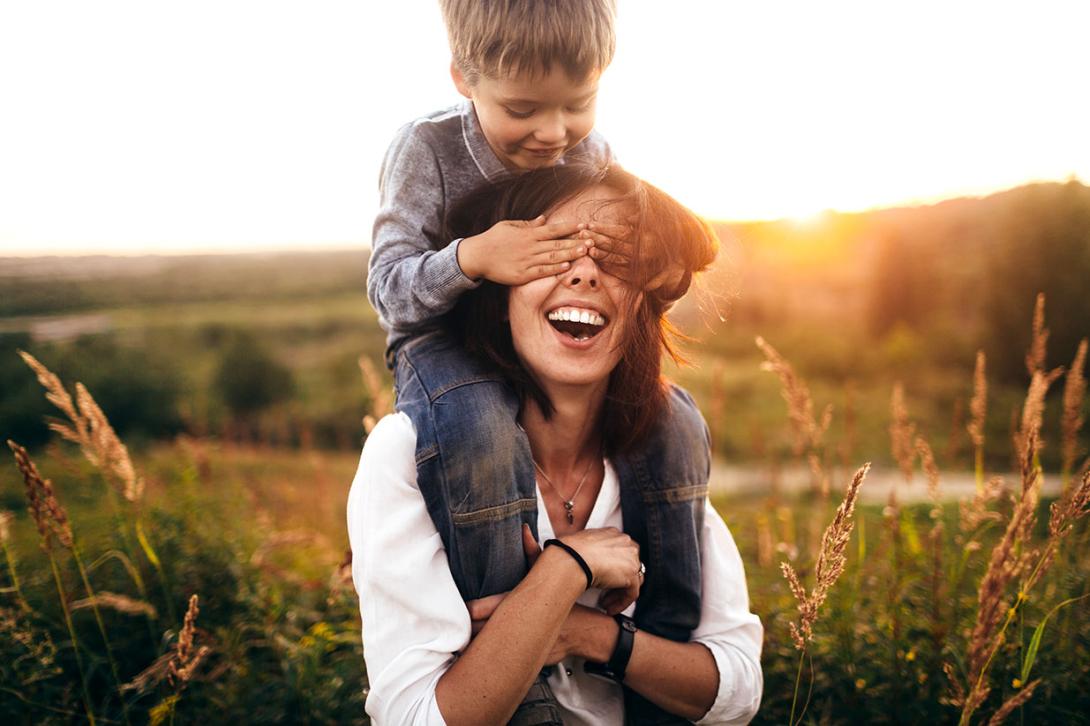 boy covering his mom's eyes in field laughing